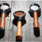Three coffee portafilters with wooden handles and metal mesh filters arranged on a rustic wooden surface, with coffee grounds visible in the center portafilter.