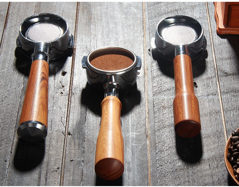 Three coffee portafilters with wooden handles and metal mesh filters arranged on a rustic wooden surface, with coffee grounds visible in the center portafilter.