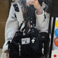 Black handbag with decorative charms held by a person wearing a white jacket.