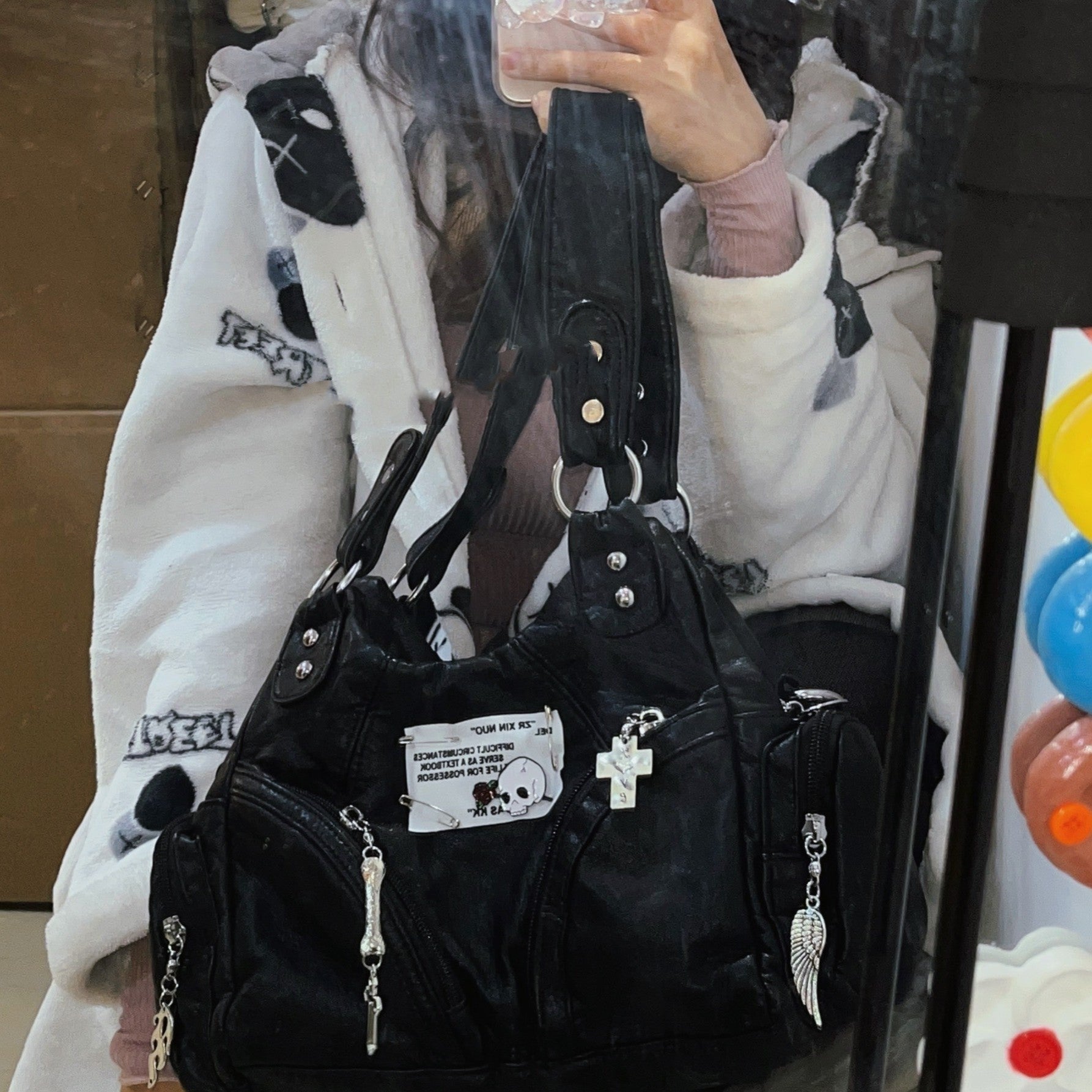 Black handbag with decorative charms held by a person wearing a white jacket.